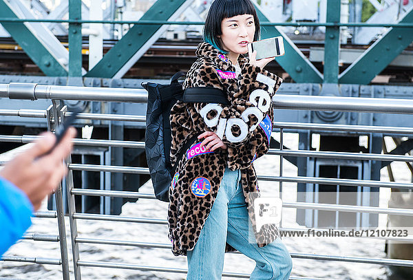Stilvolle junge Frau telefoniert mit einem Smartphone beim Spaziergang auf der Millennium-Fußgängerbrücke  London  UK