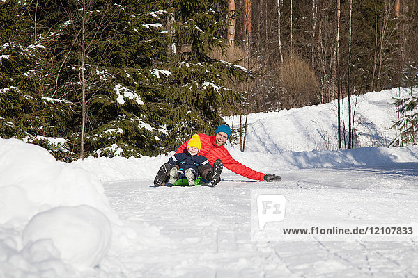 Man and son tobogganing in snow covered forest
