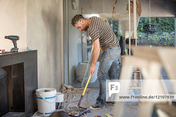 Two men in unfurnished home decorating using paint roller