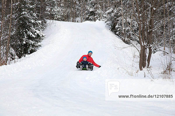 Man and son tobogganing down hill in snow covered forest