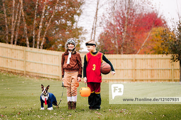 Porträt eines Jungen  einer Zwillingsschwester und eines Boston Terriers in Halloween-Kostümen im Garten