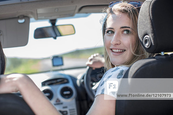 Junge Frau  die Auto fährt  über die Schulter schaut und lächelt