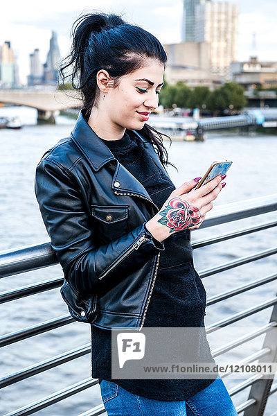 Junge Frau betrachtet ein Smartphone auf der Millennium Footbridge  London  UK