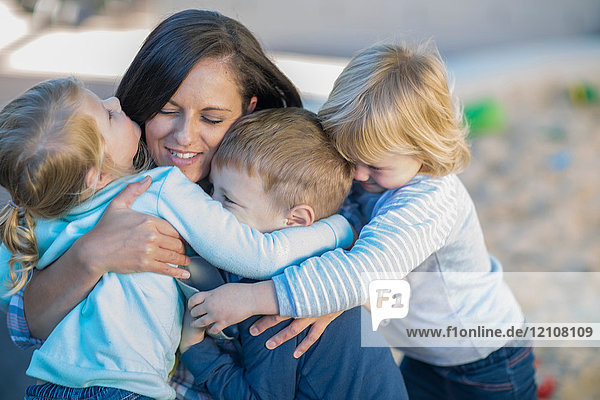 Mittlere erwachsene Frau umarmt drei kleine Kinder