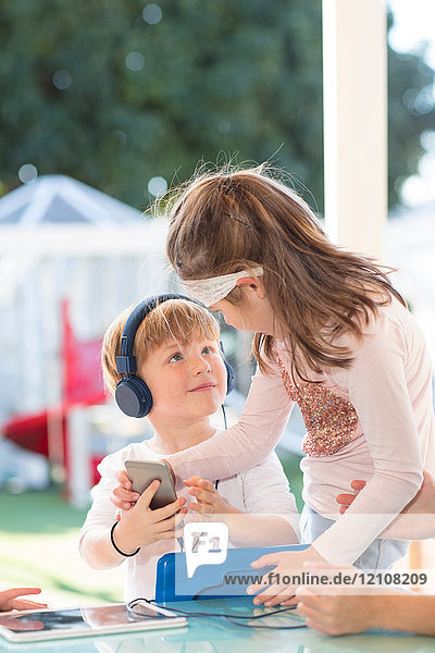 Zwei kleine Kinder halten ein Smartphone in der Hand  ein Junge trägt Kopfhörer