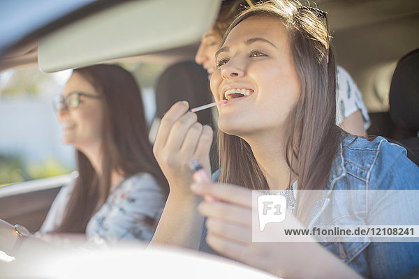 Junge Frau im Auto mit zwei Freunden  schaut in den Rückspiegel  trägt Lipgloss auf