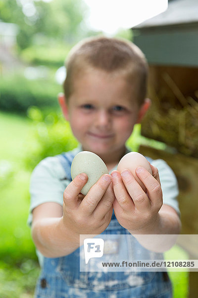 Boy holding hens eggs looking at camera smiling