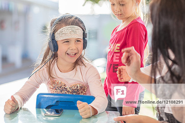 Mid adult woman sitting with young children  young girl using smartphone  wearing headphones