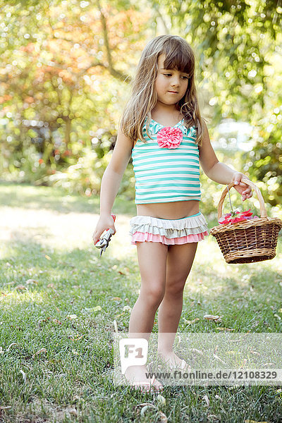 Mädchen trägt Korb mit Schnittblumen und Gartenschere