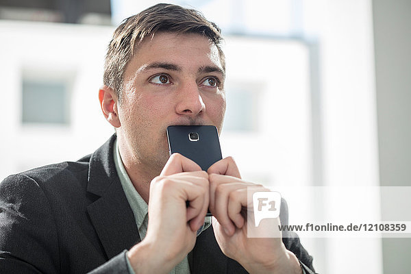 Businessman holding smartphone over mouth looking away