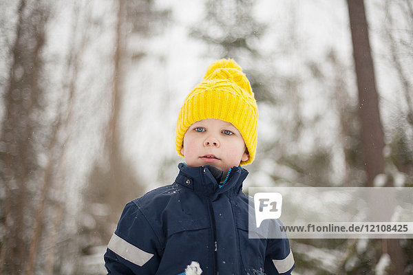 Junge mit gelber Strickmütze in schneebedecktem Wald