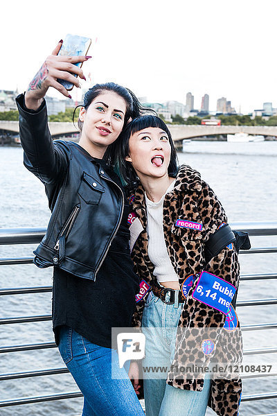 Zwei junge stilvolle Frauen beim Smartphone-Selfie auf der Millennium Footbridge  London  UK