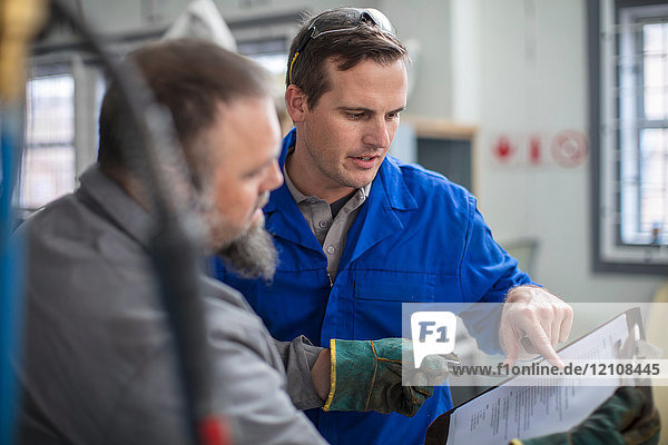 Männliche Automechaniker zeigen auf das Klemmbrett in der Reparaturwerkstatt