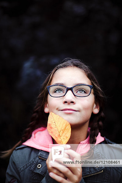 Portrait of girl with plaits and glasses holding leaf