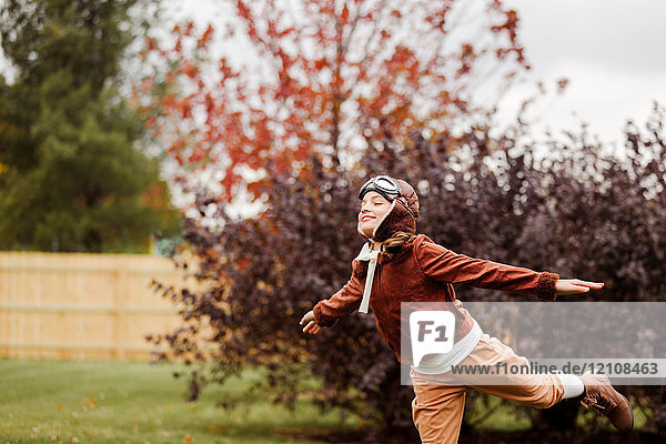 Girl wearing pilot costume for halloween with arms open in park