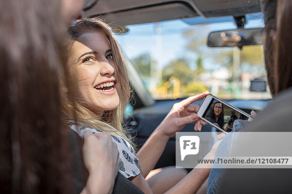 Drei Frauen im Auto  die sich ein Smartphone anschauen