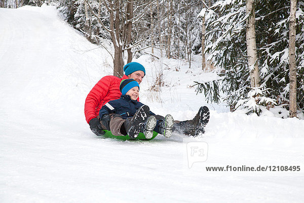 Man and son tobogganing down hill in snow covered forest