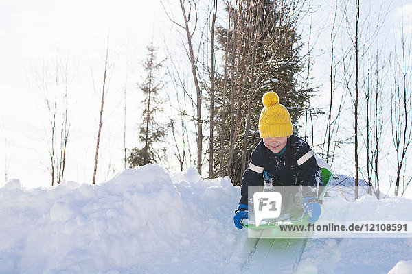 Boy in yellow knit hat tobogganing on snow covered hill