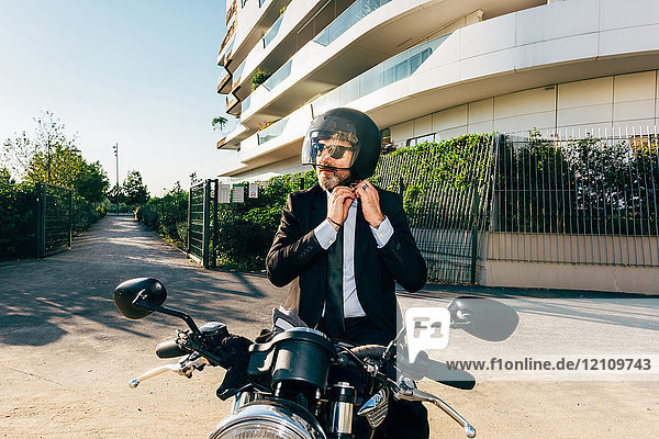 Mature businessman outdoors  sitting on motorcycle  putting on motorcycle helmet