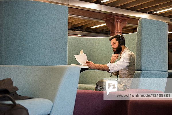Seitenansicht eines Mannes in einer Kabine mit Kopfhörern  der sich Papierkram ansieht