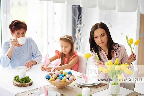 Frau mit Tochter und Mutter arrangiert gelbe Tulpen am Ostertisch