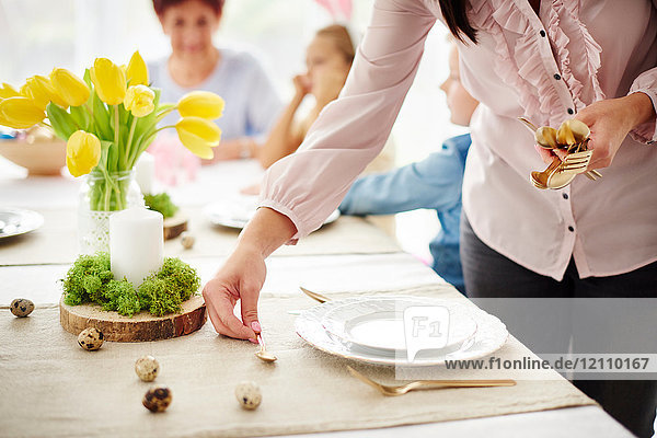 Frau und Familie bereiten Tischgedecke am Ostertisch vor