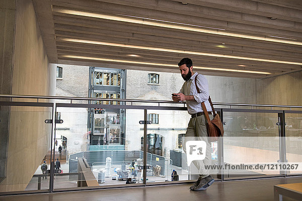 Mann im Zwischengeschoss eines Bürogebäudes schreibt auf Smartphone