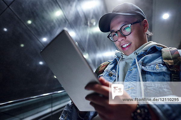 Junger Mann fährt die Rolltreppe der U-Bahn-Station hinunter und sieht sich ein digitales Tablett an