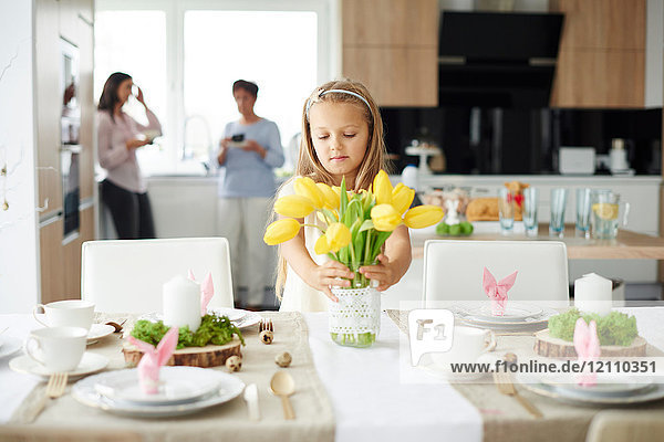 Mädchen arrangiert gelbe Tulpen am Ostertisch
