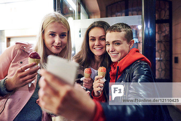 Drei junge Frauen mit Eiswaffeln nehmen Smartphone-Selfie mit auf die Straße