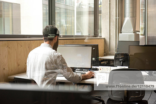 Rear view of man in office using desktop computer