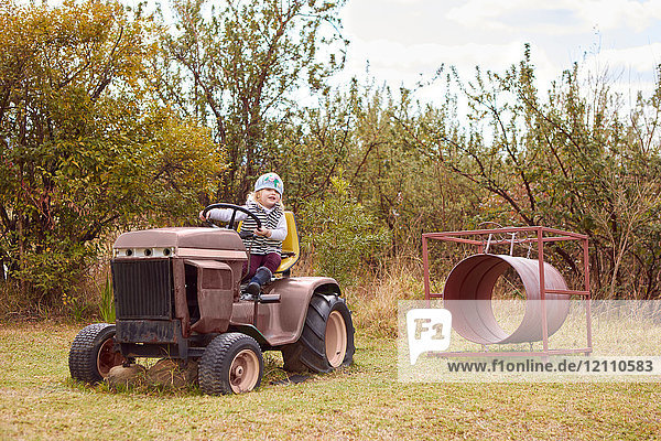 Junges Mädchen auf dem Traktor sitzend  in ländlicher Umgebung