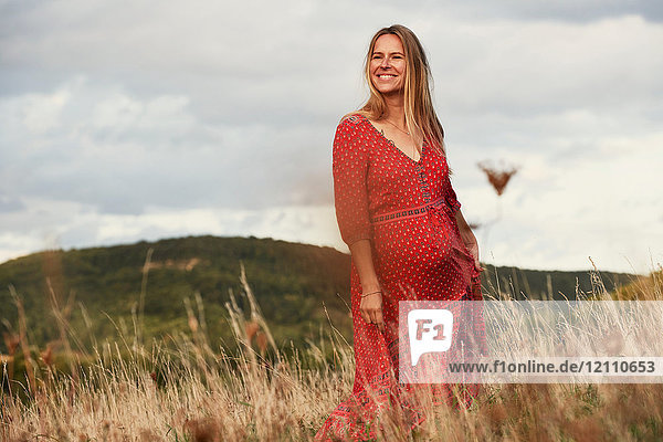 Porträt einer glücklichen schwangeren Frau in rotem Kleid am Hang