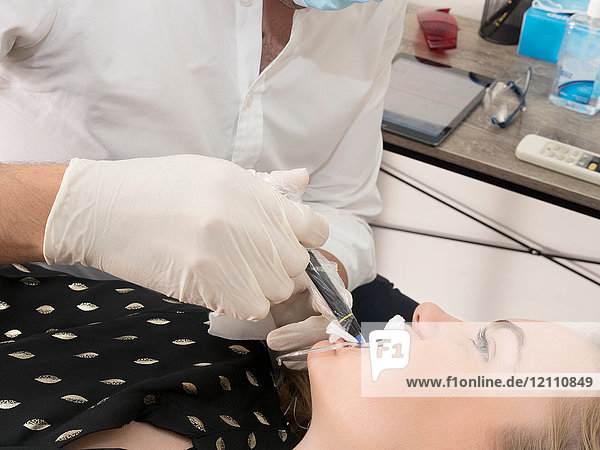 Junge Frau auf Zahnarztstuhl  Zahnarzt bereitet Frau auf zahnärztlichen Eingriff vor