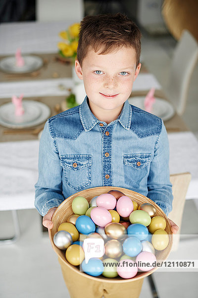 Porträt eines Jungen  der eine Schale mit bunten Ostereiern hält