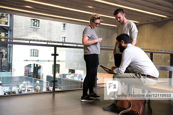 Mann mit Kollegen im Zwischengeschoss eines Bürogebäudes mit digitalem Tablet