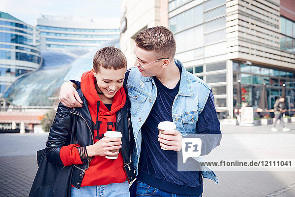 Romantisches junges Paar mit Kaffee zum Mitnehmen geht gemeinsam in der Stadt spazieren