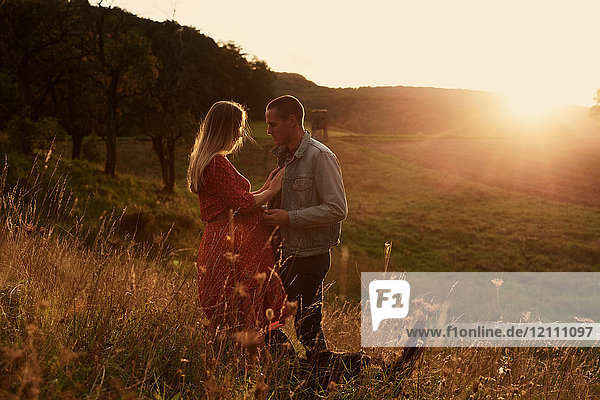 Romantisches schwangeres Paar im mittleren Erwachsenenalter von Angesicht zu Angesicht am Hang bei Sonnenuntergang