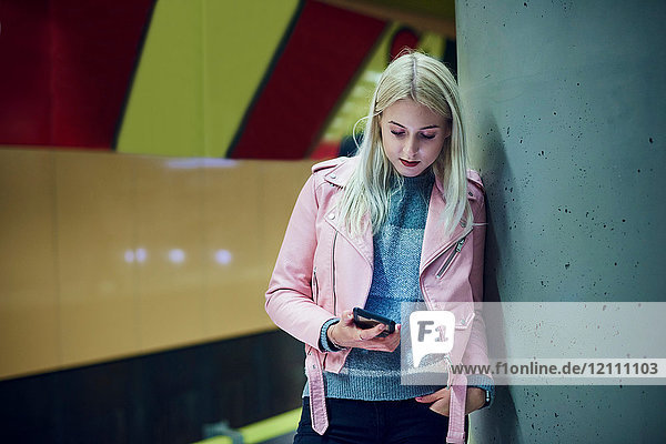 Junge Frau wartet in U-Bahn-Station und schaut auf Smartphone