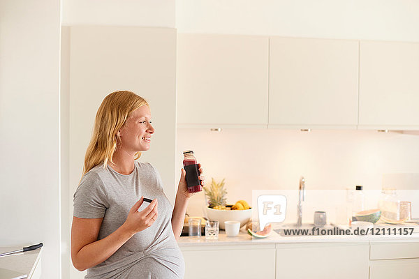 Schwangere junge Frau in der Küche mit einer Flasche Fruchtsaft
