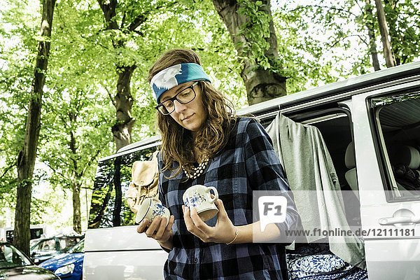 Weibliche Standinhaberin betrachtet gebrauchte Pokale am Stand auf dem Waldflohmarkt