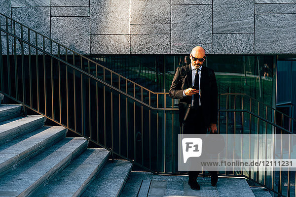 Ein reifer Geschäftsmann  der auf Stufen steht und ein Smartphone benutzt