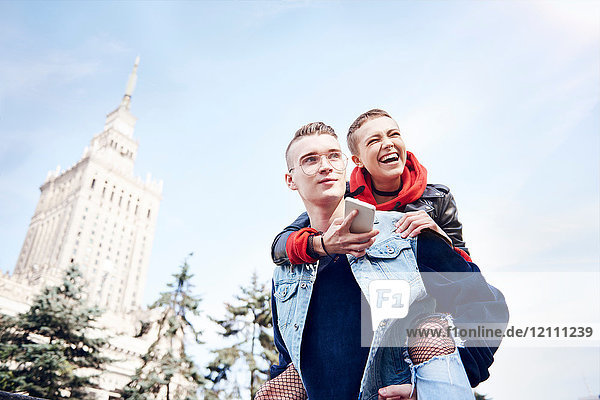 Junger Mann gibt lachender Freundin in der Stadt ein Huckepack