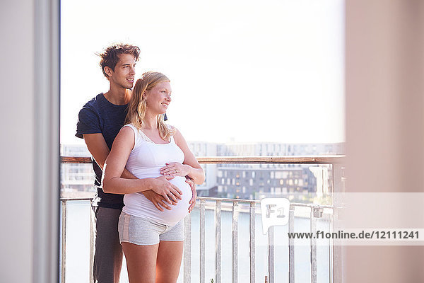 Schwangeres Paar schaut vom Balkon der Wohnung am Wasser aus