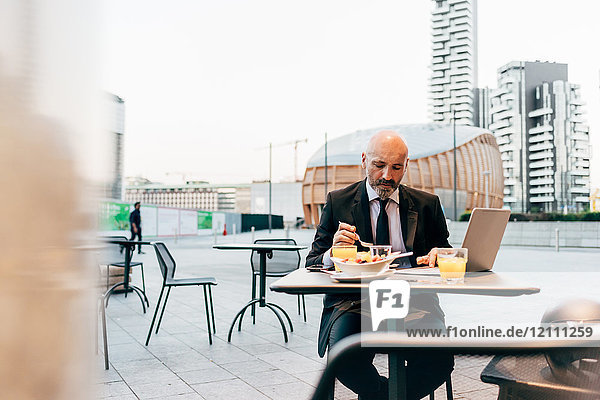 Ein reifer Geschäftsmann sitzt draußen im Café und benutzt einen Laptop