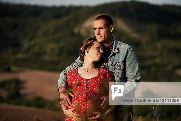 Romantischer Mann mit Händen auf dem Bauch der schwangeren Frau in der Landschaft