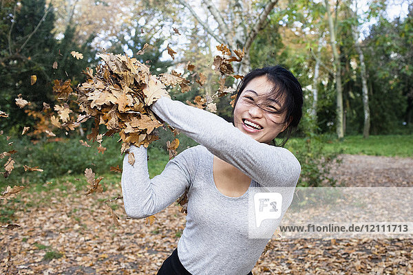 Porträt einer jungen Frau  die im Herbst im Park steht und trockene Blätter wirft.