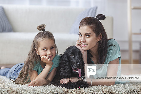 Portrait of mother and daughter lying with dog on rug at home