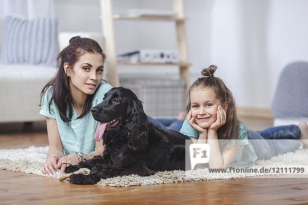 Porträt von Mutter und Tochter liegend mit Hund auf Teppich zu Hause