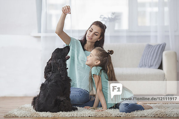 Mutter und Tochter spielen mit Hund im Wohnzimmer zu Hause